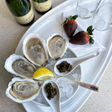 Platter of oysters on ice with caviar, lemon, and chocolate-covered strawberries, accompanied by bottles of champagne.